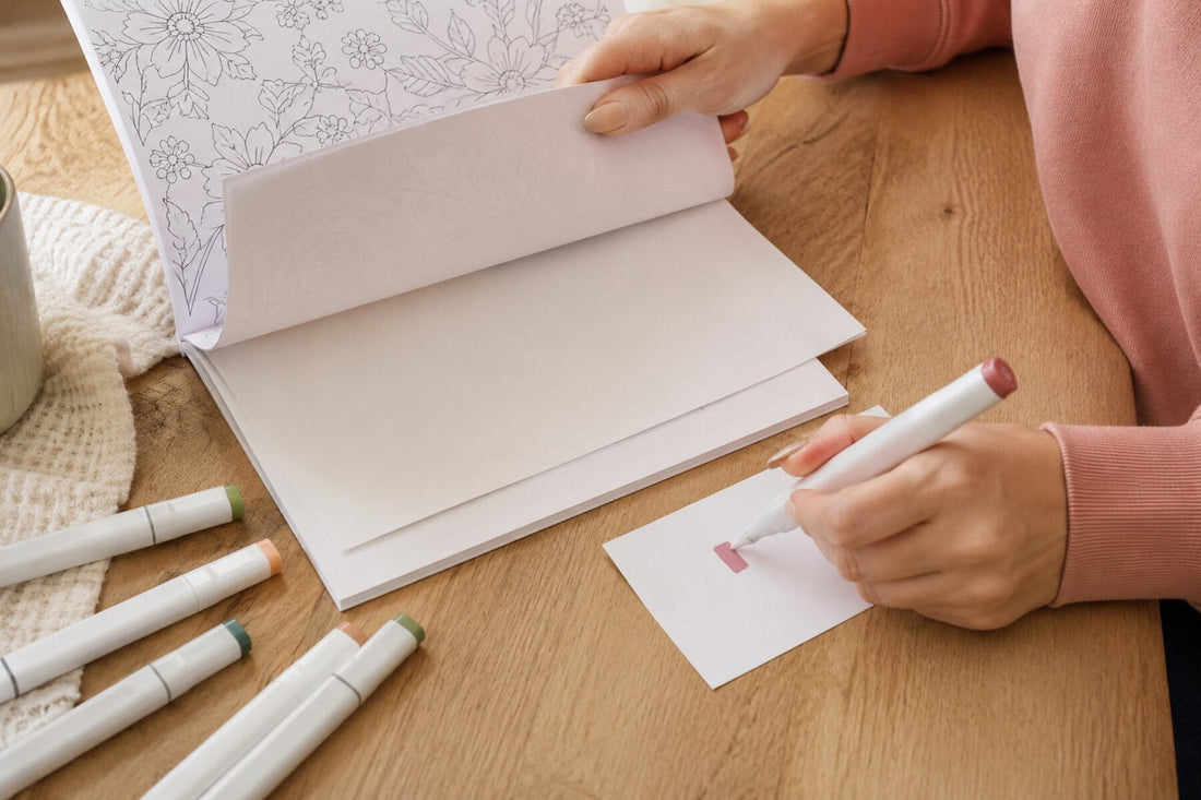 Colorist testing a marker on scrap paper with a protective sheet behind a coloring page