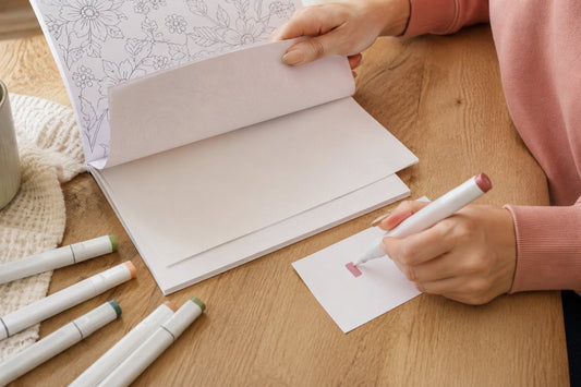 Colorist testing a marker on scrap paper with a protective sheet behind a coloring page